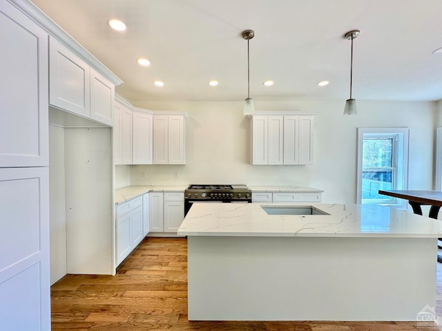 kitchen with hanging light fixtures, high end stainless steel range, light hardwood / wood-style flooring, light stone countertops, and white cabinetry