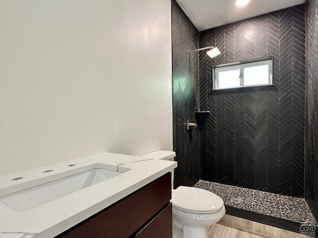 bathroom with tiled shower, vanity, wood-type flooring, and toilet