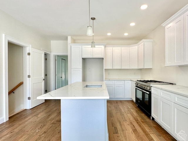 kitchen featuring light stone countertops, white cabinetry, decorative light fixtures, range with two ovens, and light wood-type flooring