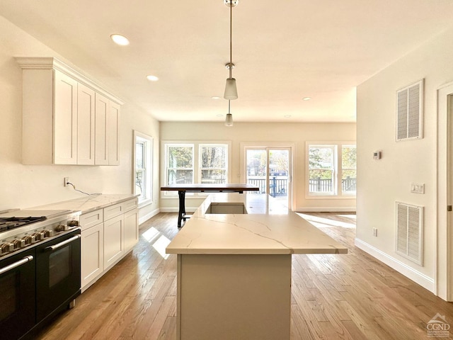 kitchen with light stone countertops, a center island, light hardwood / wood-style floors, decorative light fixtures, and range