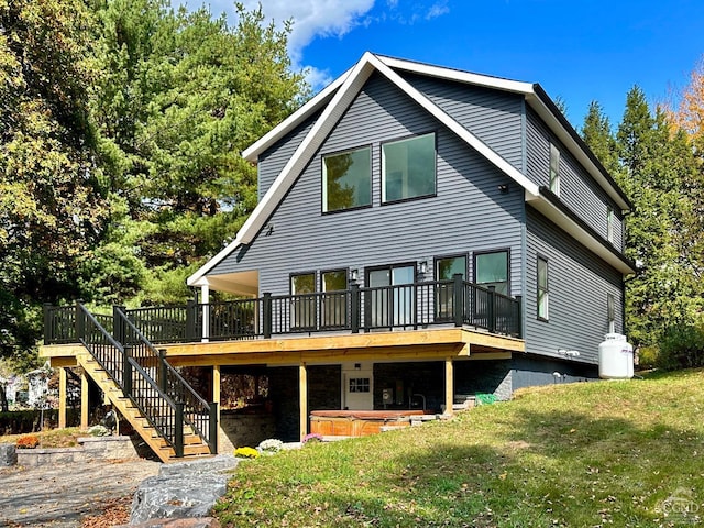 rear view of house featuring a hot tub, a deck, and a lawn