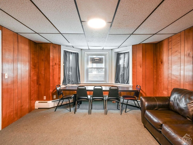 living area featuring a baseboard heating unit, a paneled ceiling, wooden walls, and carpet flooring