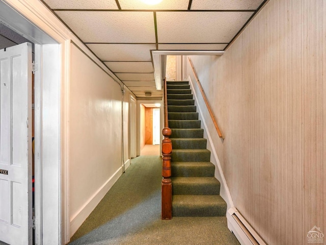 stairway featuring a paneled ceiling, baseboard heating, and carpet flooring