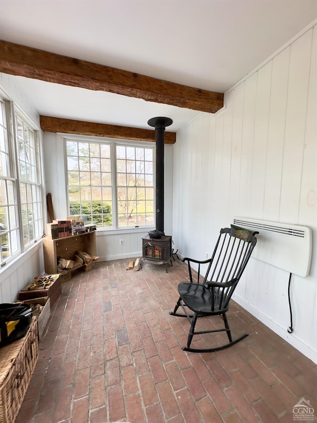 living area with beamed ceiling, plenty of natural light, a wood stove, and brick floor