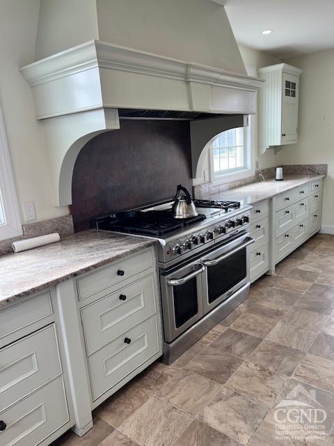 kitchen featuring light stone countertops, white cabinetry, and range with two ovens