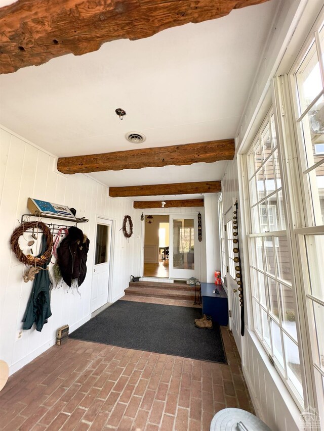 interior space with brick floor, beamed ceiling, a healthy amount of sunlight, and visible vents
