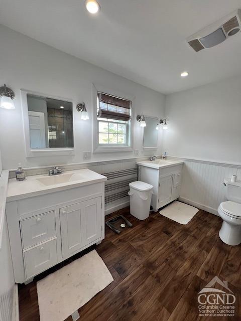 bathroom featuring toilet, wood finished floors, wainscoting, and a sink