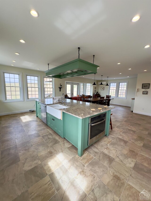 kitchen with a sink, open floor plan, an island with sink, appliances with stainless steel finishes, and green cabinetry