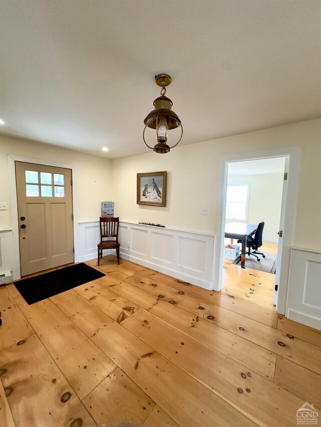 entrance foyer with light wood-style flooring, wainscoting, and a decorative wall