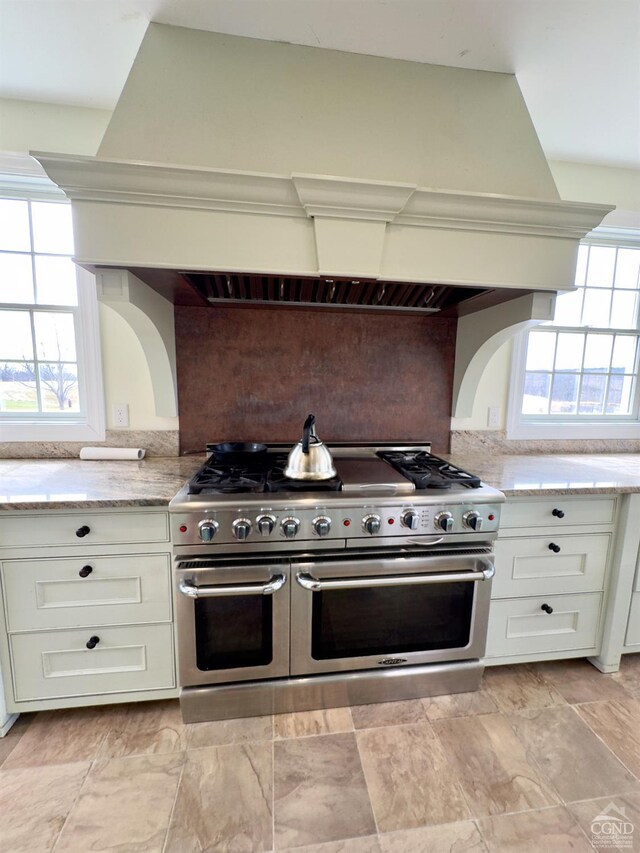 kitchen with white cabinetry, light stone counters, double oven range, and backsplash