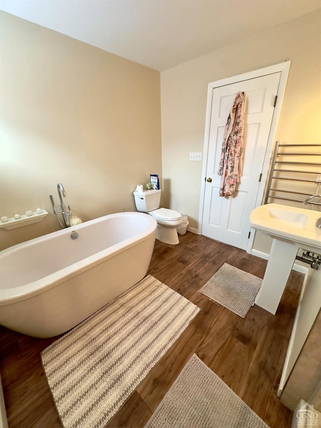 bathroom featuring baseboards, toilet, wood finished floors, and a soaking tub