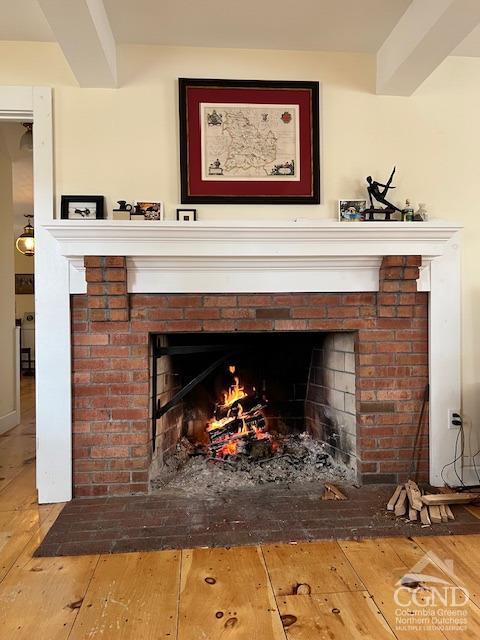 interior details featuring beamed ceiling, a brick fireplace, and wood finished floors