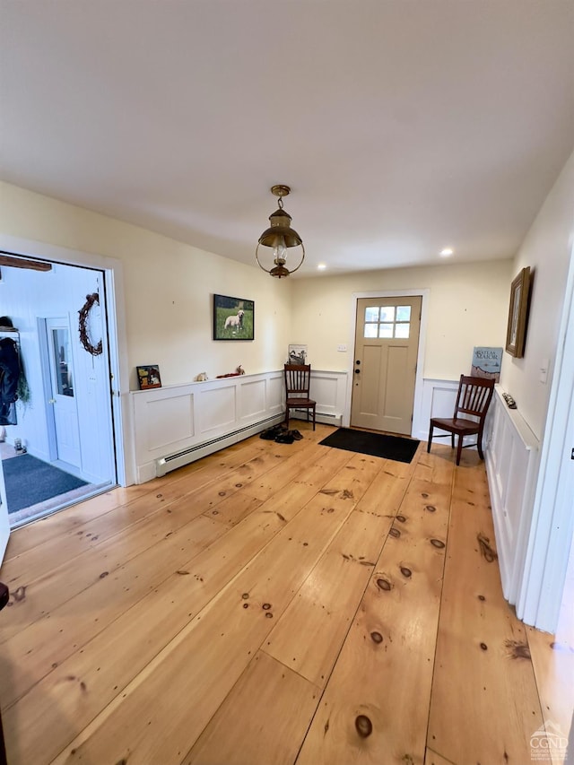 foyer entrance featuring a baseboard heating unit, light wood-style flooring, a decorative wall, and wainscoting