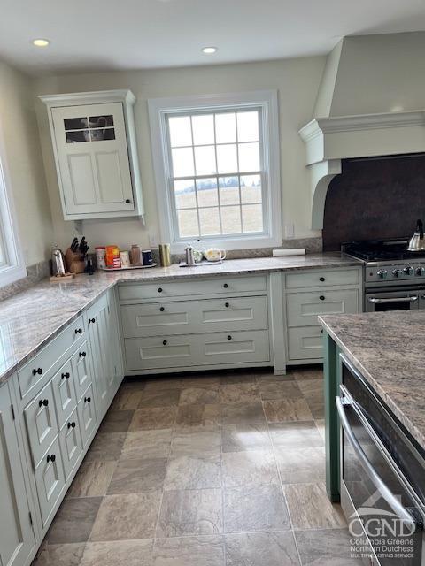 kitchen featuring light stone counters, stainless steel range with gas stovetop, wall chimney exhaust hood, and white cabinetry