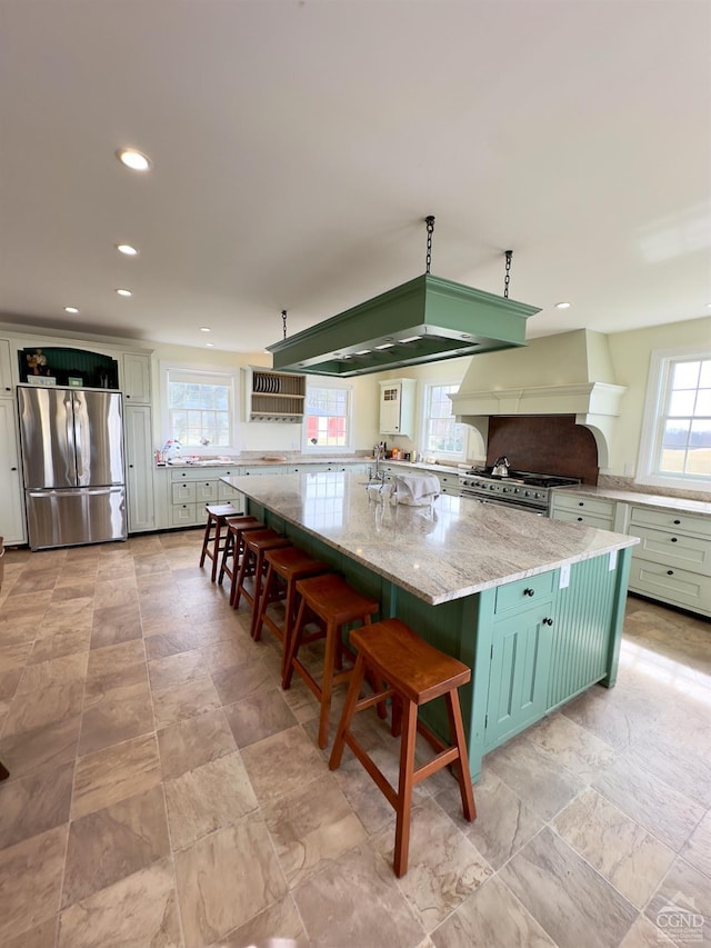 kitchen featuring light stone countertops, recessed lighting, custom range hood, appliances with stainless steel finishes, and a kitchen breakfast bar