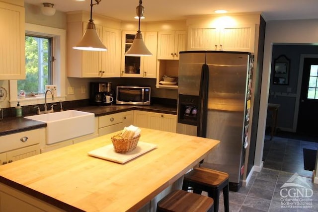 kitchen with wood counters, appliances with stainless steel finishes, sink, white cabinets, and hanging light fixtures