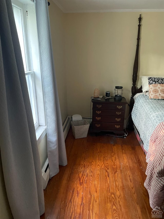 bedroom with baseboard heating, hardwood / wood-style floors, and ornamental molding