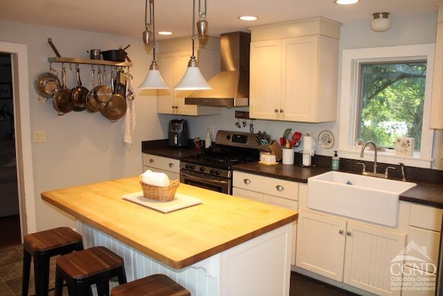 kitchen featuring wooden counters, sink, decorative light fixtures, stainless steel range oven, and custom range hood