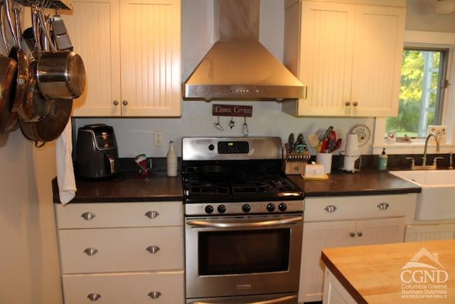 kitchen featuring wall chimney exhaust hood, white cabinetry, sink, and stainless steel range with gas stovetop