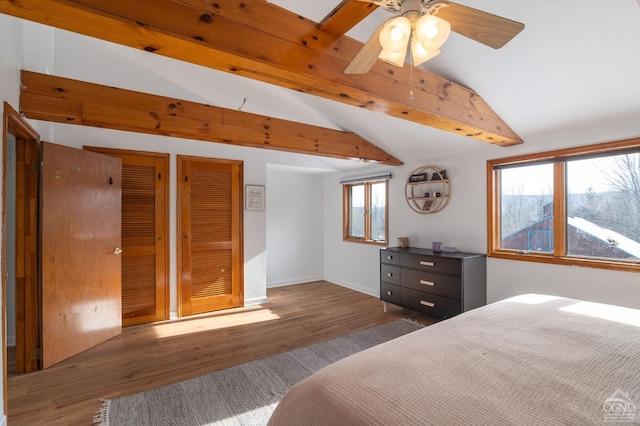 bedroom with baseboards, vaulted ceiling with beams, two closets, and wood finished floors