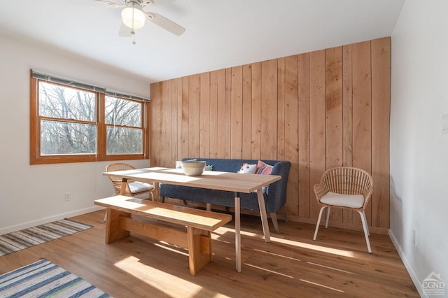 dining space featuring wood walls, ceiling fan, baseboards, and wood finished floors