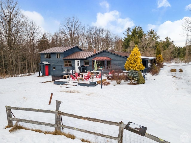 snow covered rear of property featuring a standing seam roof, metal roof, and fence