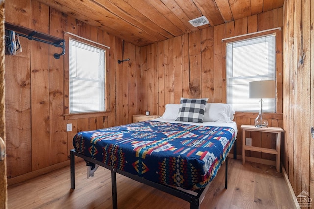 bedroom featuring wood walls, visible vents, multiple windows, and wood finished floors