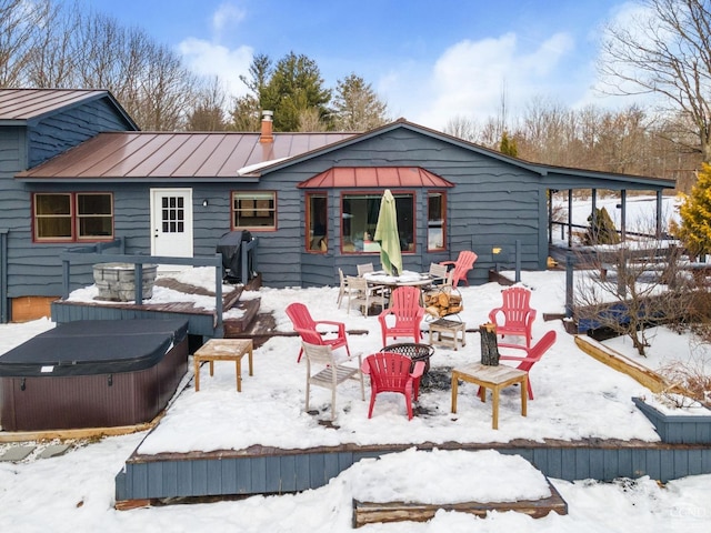 snow covered property with a standing seam roof, metal roof, an outdoor fire pit, and a hot tub