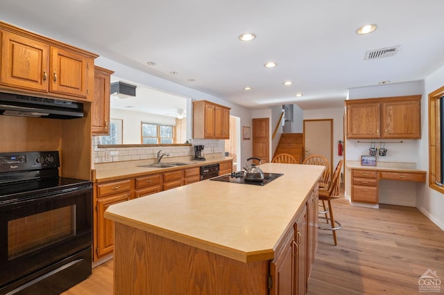 kitchen featuring a center island, black appliances, under cabinet range hood, visible vents, and a sink