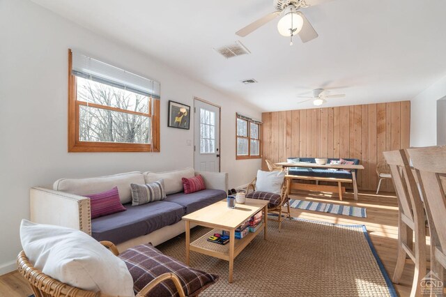 living area featuring wood walls, visible vents, a ceiling fan, and wood finished floors