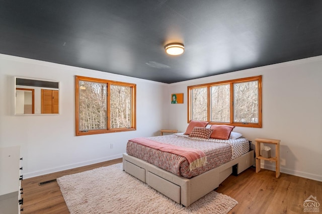 bedroom featuring wood finished floors, baseboards, ornamental molding, and visible vents