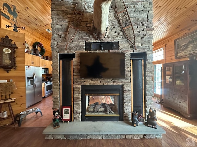 interior space featuring a stone fireplace, appliances with stainless steel finishes, hardwood / wood-style flooring, and wooden walls