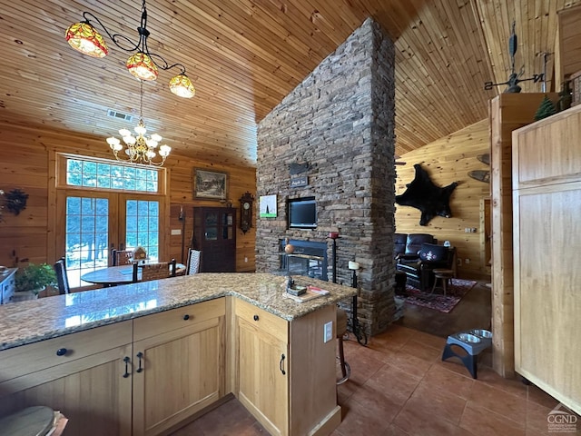 kitchen featuring wooden walls, light brown cabinets, high vaulted ceiling, pendant lighting, and light stone counters