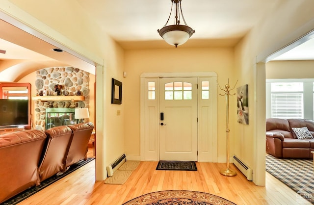 foyer entrance with baseboard heating, a stone fireplace, and hardwood / wood-style flooring