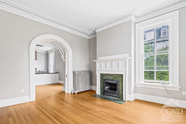 unfurnished living room featuring radiator, hardwood / wood-style flooring, plenty of natural light, and ornamental molding