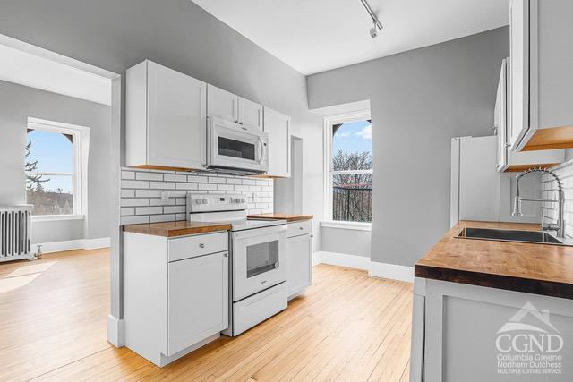 kitchen featuring white cabinetry, radiator heating unit, sink, light hardwood / wood-style flooring, and white appliances