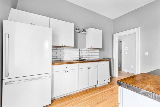 kitchen with white appliances, sink, light wood-type flooring, tasteful backsplash, and white cabinetry