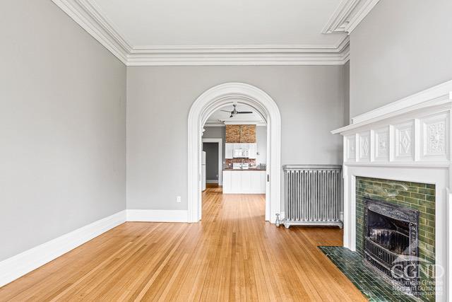 unfurnished living room with radiator, wood-type flooring, crown molding, and a tile fireplace