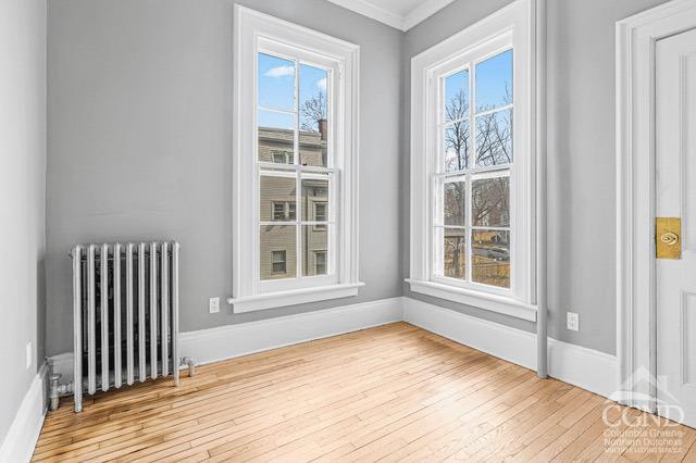 empty room with light hardwood / wood-style flooring, radiator, a healthy amount of sunlight, and crown molding