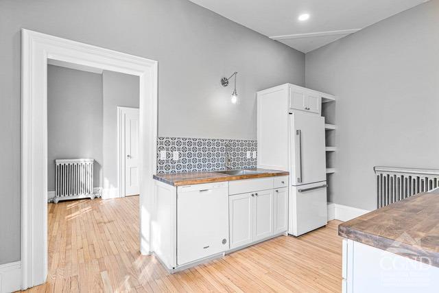 kitchen with sink, radiator heating unit, high end fridge, white cabinets, and light wood-type flooring