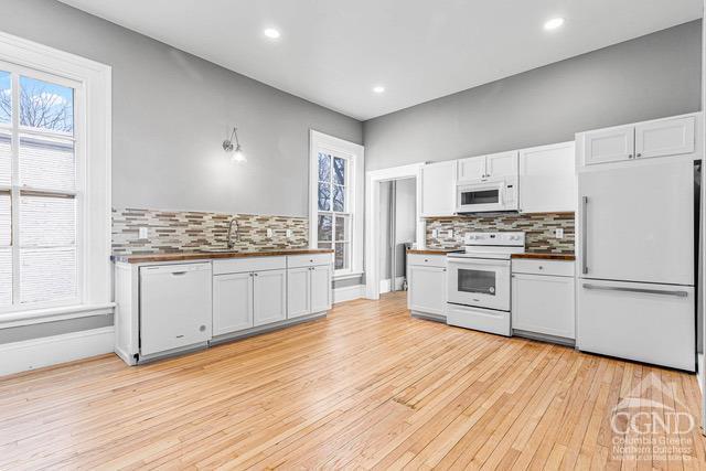 kitchen with white cabinets, light hardwood / wood-style floors, white appliances, and sink