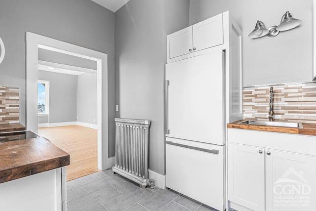 kitchen featuring tasteful backsplash, radiator, sink, white cabinets, and white fridge