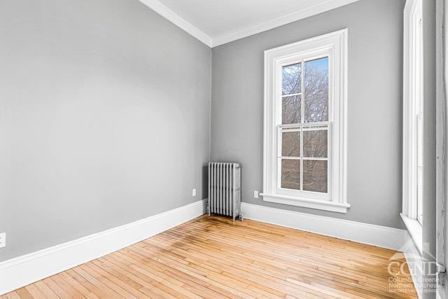 spare room with light wood-type flooring, ornamental molding, and radiator