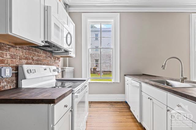 kitchen with sink, butcher block countertops, light hardwood / wood-style floors, white appliances, and white cabinets