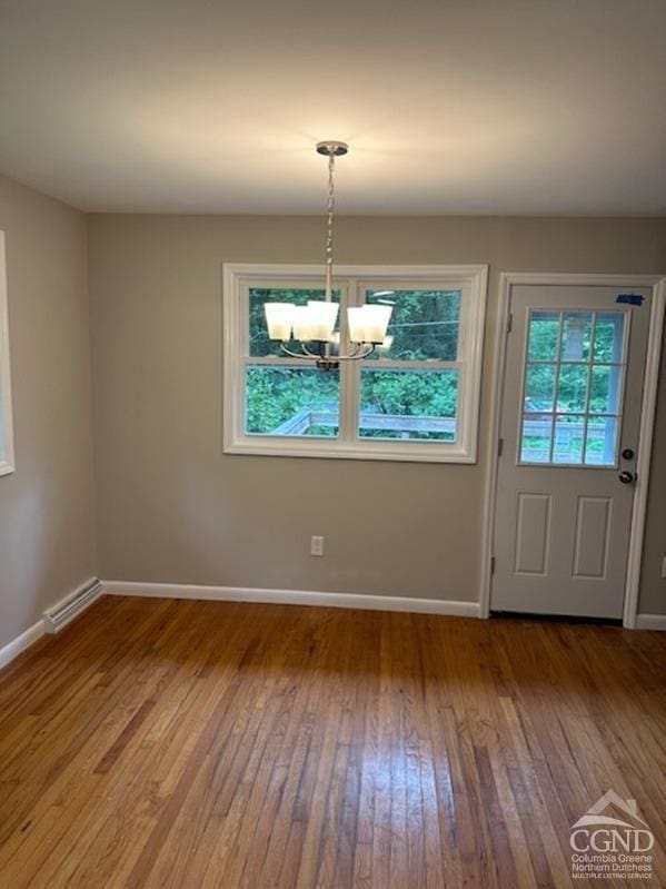 unfurnished dining area with wood-type flooring and an inviting chandelier