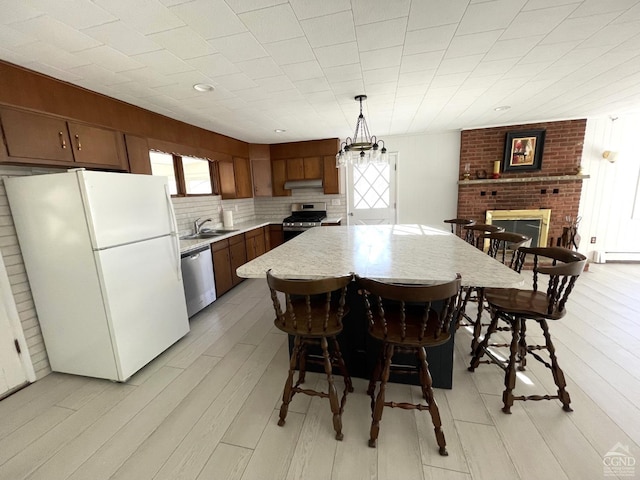 dining area featuring a baseboard heating unit, light wood-type flooring, a brick fireplace, and a notable chandelier