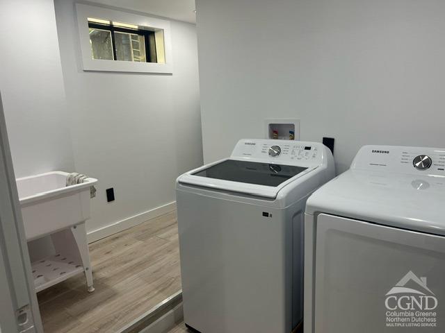 clothes washing area with washing machine and dryer and light wood-type flooring