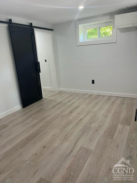 empty room featuring a wall mounted air conditioner, a barn door, and light hardwood / wood-style flooring