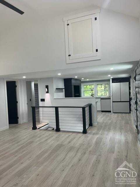 kitchen featuring stainless steel dishwasher, a towering ceiling, white fridge, white cabinets, and light wood-type flooring