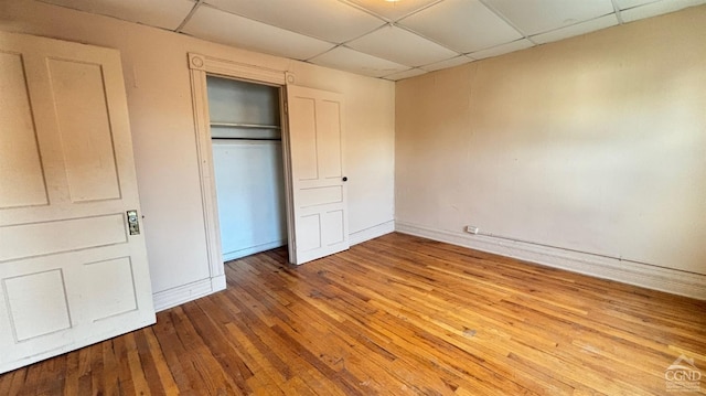 unfurnished bedroom with hardwood / wood-style floors, a paneled ceiling, and a closet